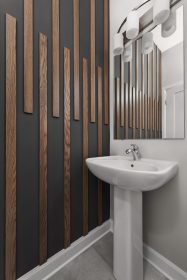 Modern powder room featuring a white pedestal sink, a dark accent wall with vertical wood slats, a rectangular mirror reflecting the slatted wall, and a sleek light fixture with cylindrical white shades