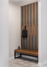 Modern mudroom with a vertical wood slat accent wall featuring metal hooks, a brown faux-leather bench with black metal legs, a black tote bag hanging on a hook, and a cup and sunglasses resting on the bench.